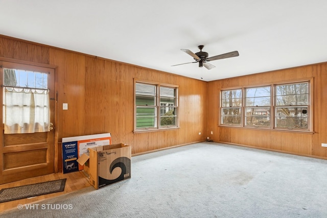 empty room featuring carpet flooring, wood walls, baseboards, and ceiling fan