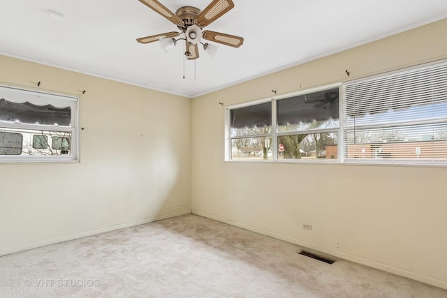 empty room featuring a ceiling fan, visible vents, carpet floors, baseboards, and crown molding