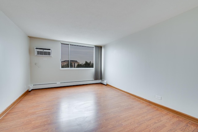 spare room featuring an AC wall unit, baseboard heating, light wood-type flooring, and baseboards