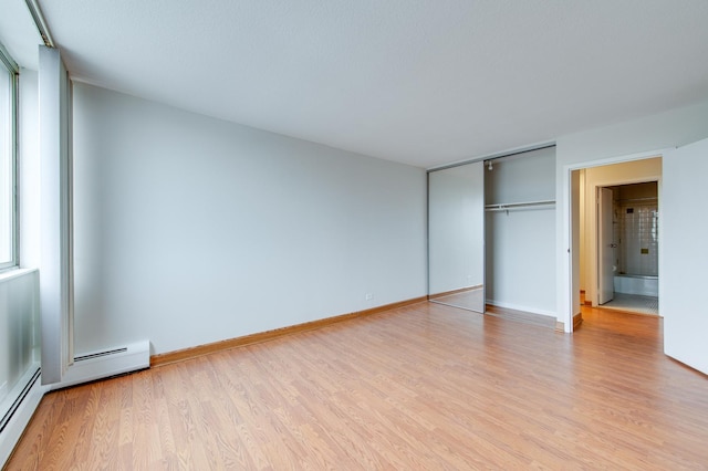 unfurnished bedroom with a closet, a baseboard heating unit, light wood-type flooring, multiple windows, and baseboards