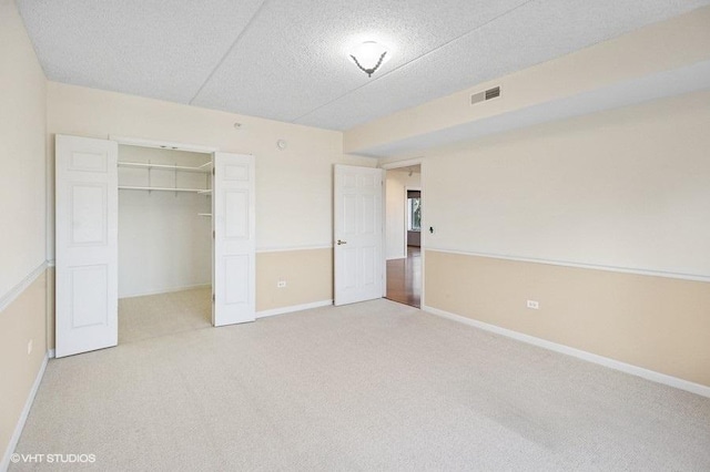 unfurnished bedroom featuring baseboards, visible vents, light colored carpet, a textured ceiling, and a closet