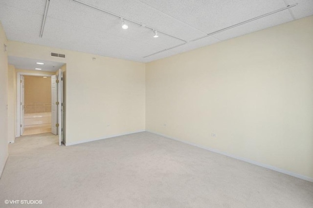 spare room featuring baseboards, visible vents, rail lighting, and light colored carpet