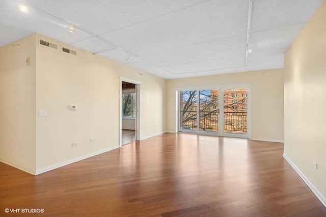 spare room featuring rail lighting, baseboards, and wood finished floors