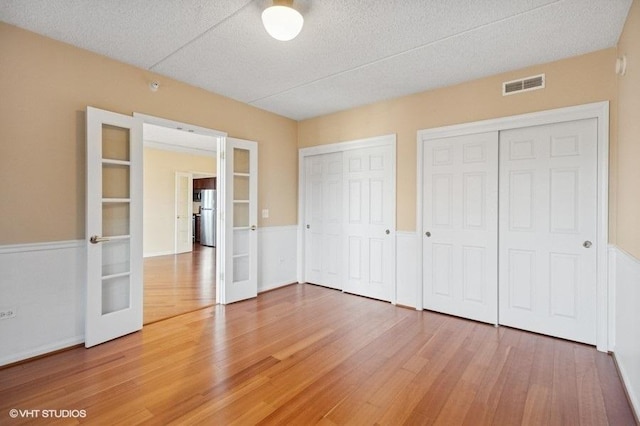 unfurnished bedroom with wood finished floors, visible vents, multiple closets, french doors, and freestanding refrigerator