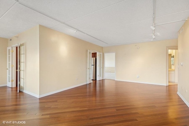 spare room featuring wood finished floors, rail lighting, and baseboards