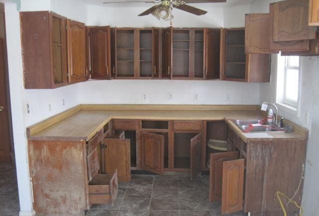 kitchen featuring a ceiling fan, brown cabinets, a sink, and glass insert cabinets