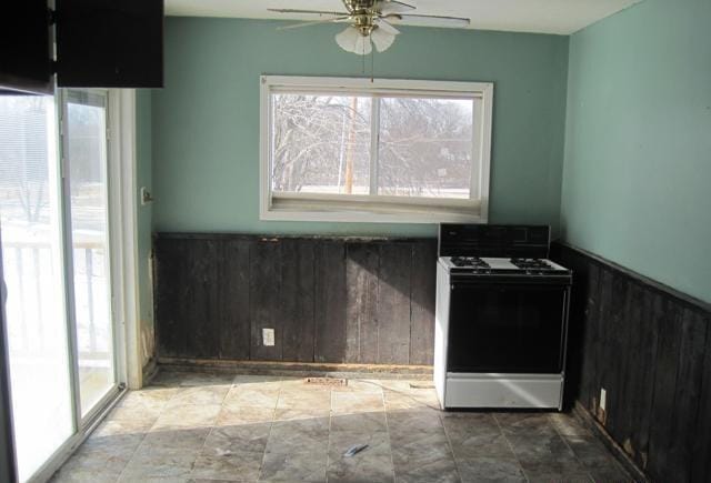 kitchen with a wainscoted wall, ceiling fan, wood walls, and gas range