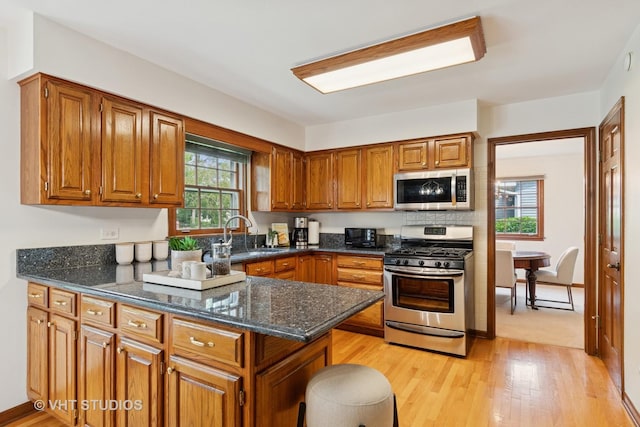 1109 E Gartner Rd, Naperville, IL 60540 - kitchen featuring appliances with stainless steel finishes, brown cabinetry, light wood finished floors, and dark stone countertops