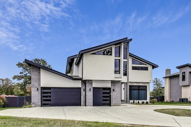 contemporary home with concrete driveway, brick siding, central air condition unit, and stucco siding