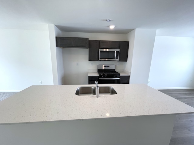 kitchen featuring light stone countertops, stainless steel appliances, a sink, and wood finished floors