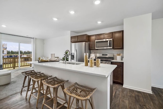 kitchen featuring dark wood-style flooring, a breakfast bar area, stainless steel appliances, recessed lighting, and a sink