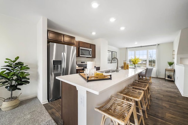 kitchen with stainless steel appliances, light countertops, a sink, dark brown cabinets, and a kitchen bar