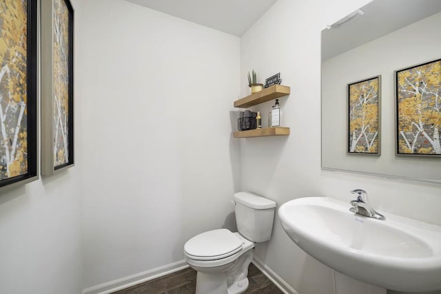 half bathroom with baseboards, a sink, toilet, and wood finished floors