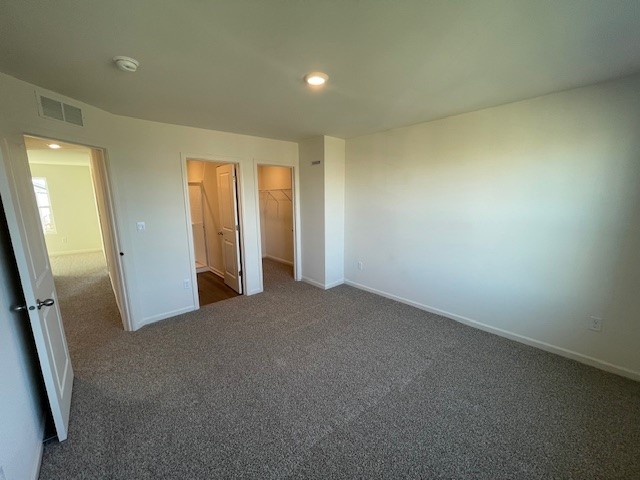 unfurnished bedroom with carpet floors, baseboards, visible vents, and a walk in closet