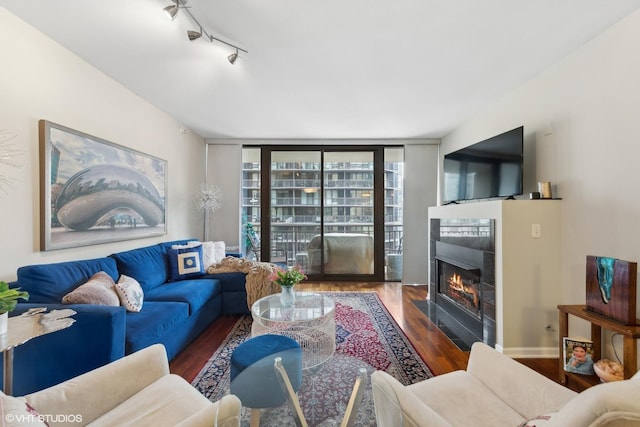 living room with baseboards, rail lighting, a tiled fireplace, and wood finished floors