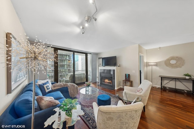 living area featuring track lighting, a tile fireplace, baseboards, and wood finished floors