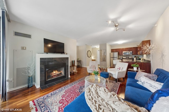 living room with a tiled fireplace, wood finished floors, visible vents, and baseboards