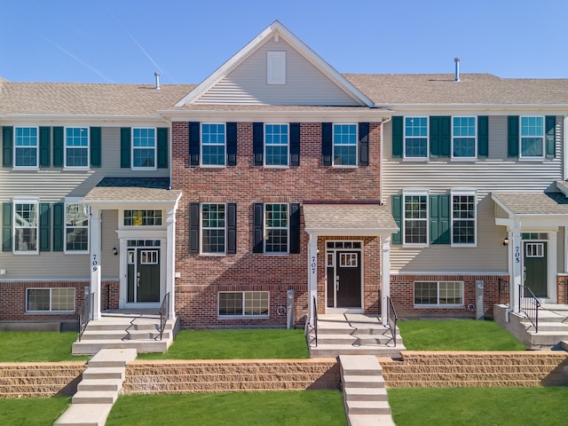 view of front of property with brick siding, a front lawn, and roof with shingles