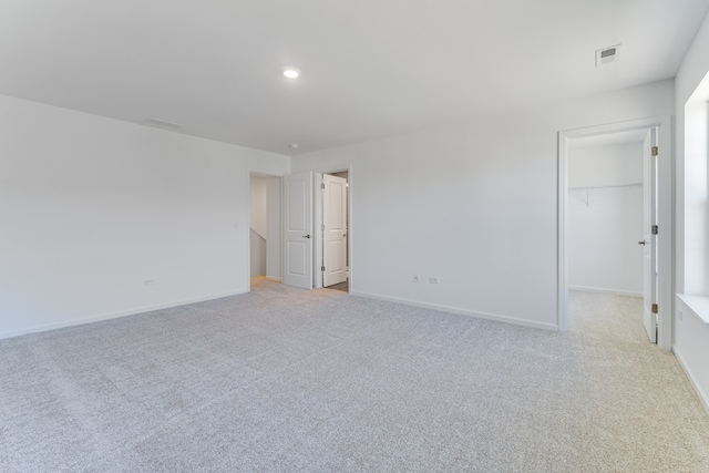 unfurnished bedroom featuring a walk in closet, recessed lighting, visible vents, light carpet, and baseboards