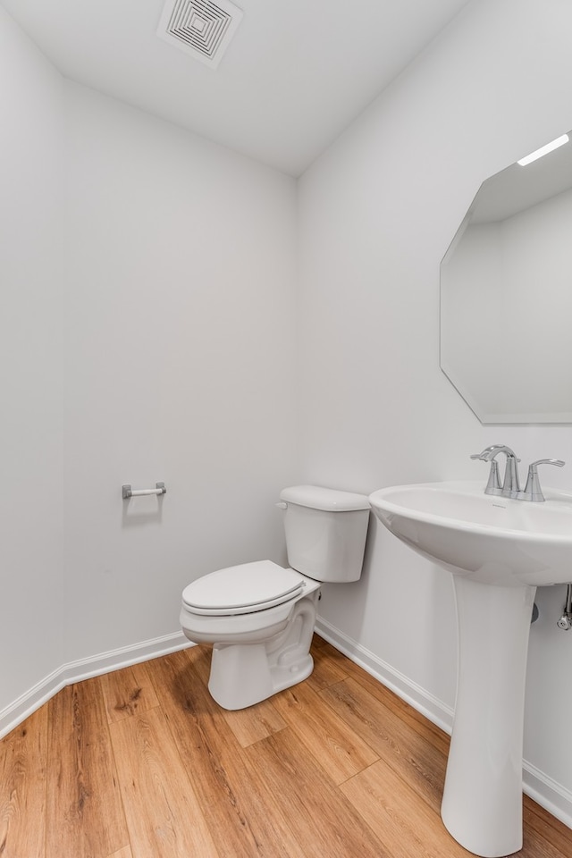 half bathroom with visible vents, toilet, a sink, wood finished floors, and baseboards