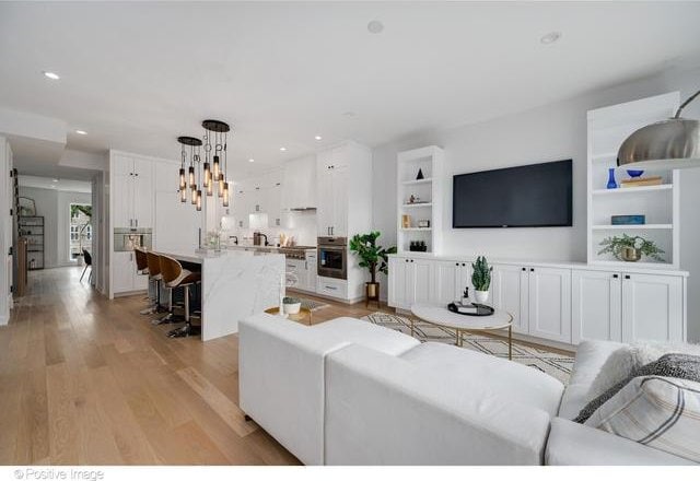 living room with built in shelves, recessed lighting, and light wood-style floors