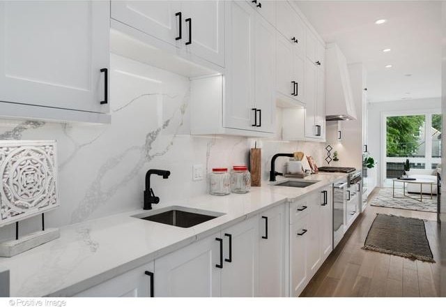 kitchen with wall chimney range hood, decorative backsplash, white cabinets, and a sink