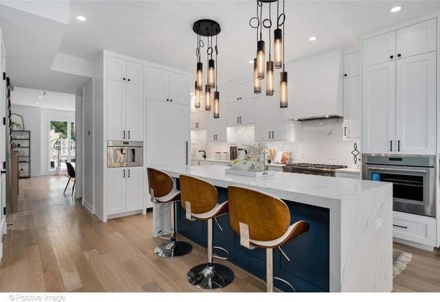 kitchen with white cabinets, appliances with stainless steel finishes, light wood-type flooring, a center island with sink, and pendant lighting