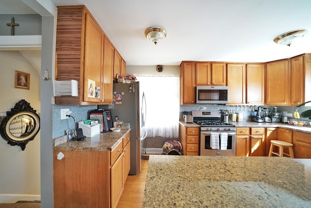 kitchen with stainless steel appliances, light wood-type flooring, brown cabinets, and tasteful backsplash