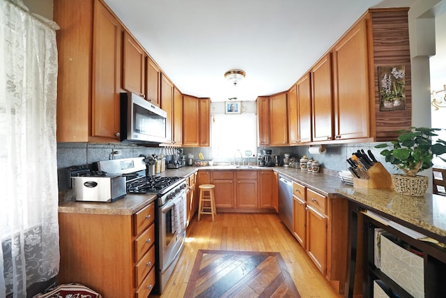 kitchen featuring light wood-style floors, tasteful backsplash, appliances with stainless steel finishes, and brown cabinets