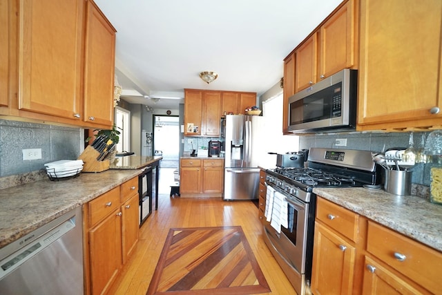 kitchen with appliances with stainless steel finishes, light wood-type flooring, backsplash, and brown cabinets