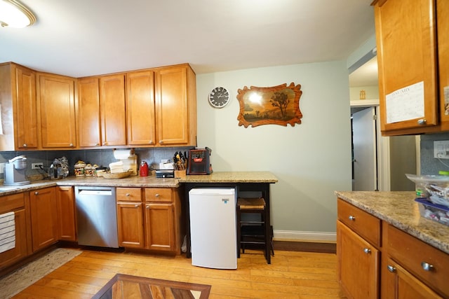 kitchen featuring refrigerator, brown cabinets, light wood finished floors, tasteful backsplash, and dishwasher