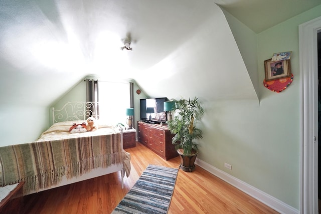 bedroom with light wood-type flooring, lofted ceiling, and baseboards