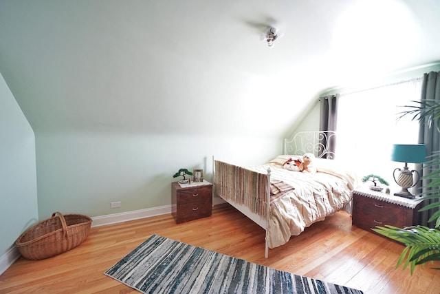 bedroom featuring lofted ceiling, wood finished floors, and baseboards