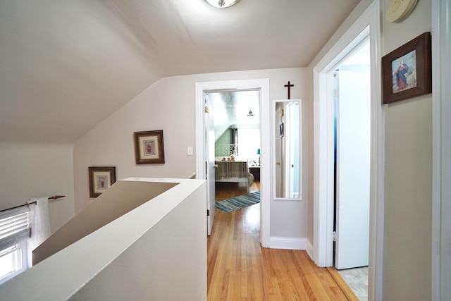 hallway featuring light wood-type flooring, baseboards, lofted ceiling, and an upstairs landing