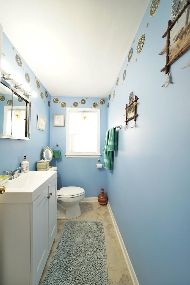 half bath with baseboards, vanity, and toilet