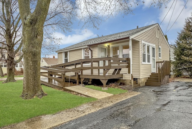 view of front of property with aphalt driveway, roof with shingles, and a front yard