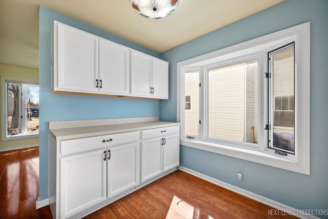 kitchen featuring light countertops, white cabinets, baseboards, and wood finished floors