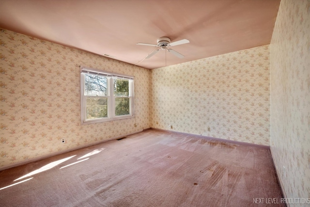 carpeted empty room featuring baseboards, a ceiling fan, visible vents, and wallpapered walls