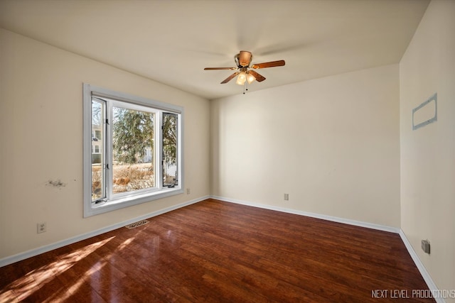 spare room with dark wood-type flooring, a ceiling fan, visible vents, and baseboards