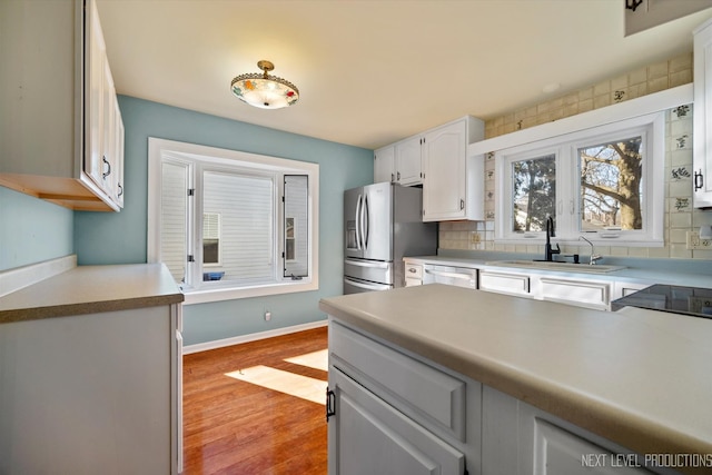 kitchen with decorative backsplash, white cabinets, a sink, light wood-type flooring, and stainless steel fridge with ice dispenser