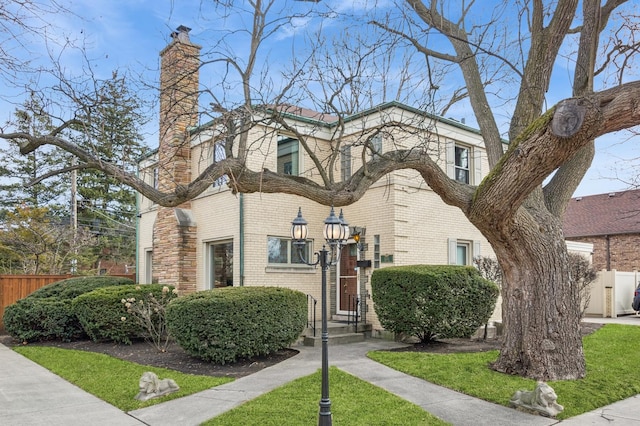 view of front of property featuring brick siding, a chimney, and fence