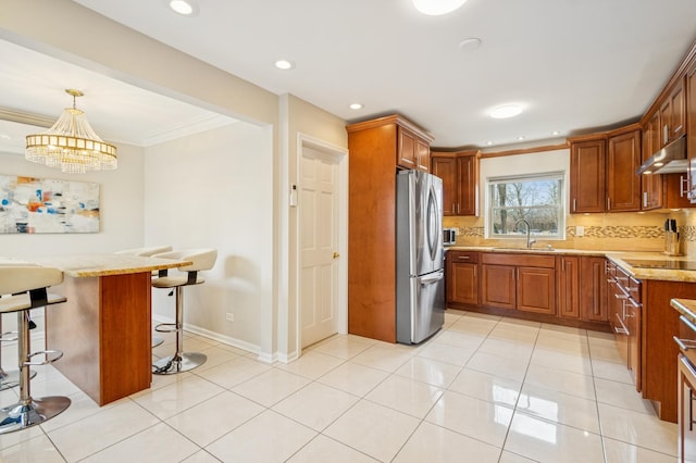 kitchen featuring light tile patterned floors, decorative backsplash, freestanding refrigerator, a sink, and under cabinet range hood