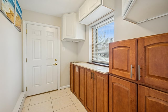 interior space with brown cabinets, a baseboard heating unit, white cabinets, light tile patterned flooring, and baseboards