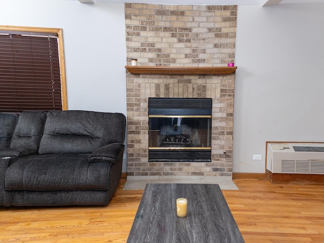 living area featuring a brick fireplace, baseboards, and wood finished floors