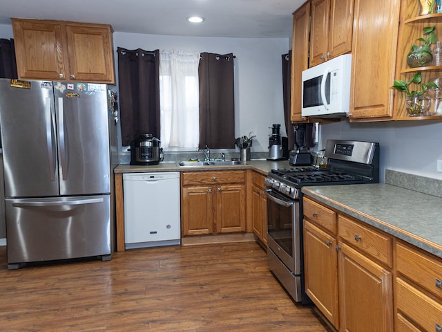 kitchen featuring appliances with stainless steel finishes, brown cabinets, dark wood-style flooring, a sink, and recessed lighting