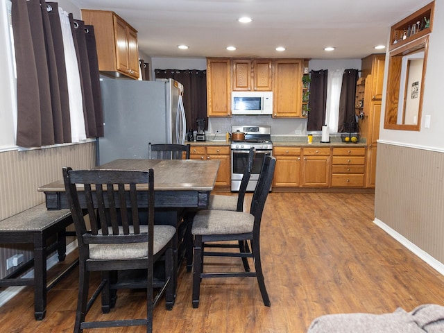 kitchen with a wainscoted wall, stainless steel appliances, wood finished floors, and recessed lighting