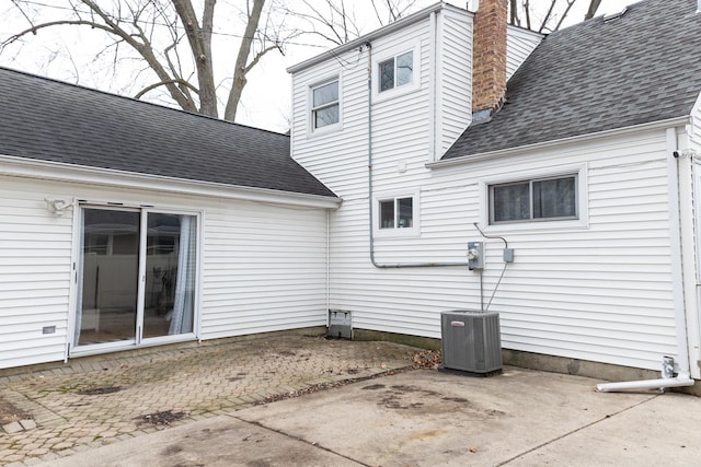 rear view of property with a shingled roof, a chimney, cooling unit, and a patio