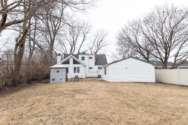 back of property featuring a chimney, fence, and a lawn