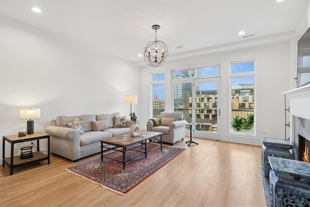 living room with recessed lighting, a premium fireplace, visible vents, light wood finished floors, and an inviting chandelier