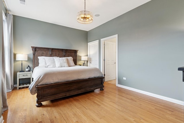 bedroom featuring baseboards, an inviting chandelier, visible vents, and light wood-style floors